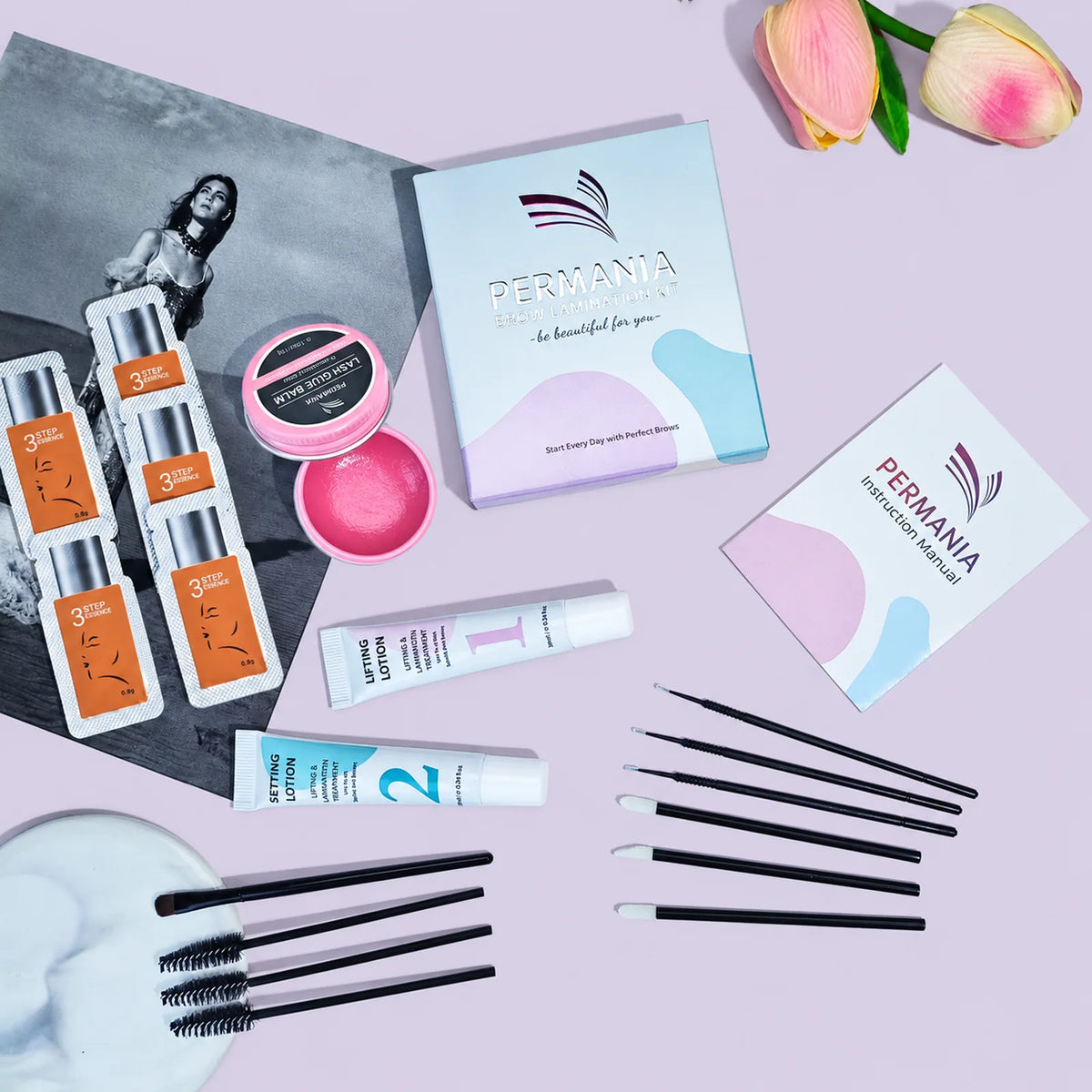 Flat lay of the PERMANIA brow lamination kit with box, instruction manual, lotions, essence sachets, glue balm and applicator brushes.