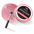 Open and closed pink PERMANIA lash glue balm jars with a flat applicator brush on a white background.